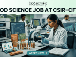 CSIR-CFTRI Recruitment 2026 Exciting Food Science Job Opening in Mysuru "A detailed, professional featured image banner for a job page. At the top, a white header band displays the Biotecnika logo (the black text and leaf-icon from image_15.png reading 'biotecnika Your Bio Resource') above a large, bold black headline, 'FOOD SCIENCE JOB AT CSIR-CFTRI'. Below the header is a realistic photograph of a modern, bustling, well-equipped food science research laboratory. In the foreground, a female scientist of South Asian descent in a lab coat is carefully looking through a compound microscope. Behind her and at a separate station, an older male scientist works with advanced high-performance liquid chromatography (HPLC) analytical equipment and another computer, while a younger male scientist analyzes data on a large monitor. The workbench is covered with various ingredient vials, packaged 'Fortified Grains' and 'Novel Protein Bar' prototypes, and computers displaying complex data graphs, molecular structures, and composition charts. A lab notebook with doodles is also present. At the very bottom, a solid teal footer bar features a prominent call-to-action button with white text that reads 'APPLY NOW' with a right-pointing arrow."