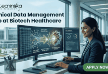 Clinical Data Management Job at Biotech Healthcare | Apply Online Here Clinical Data Management Job at Biotech Healthcare Apply Online Here. A corporate job advertisement for a "Clinical Data Management Job at Biotech Healthcare," featuring a professional female of South Asian descent smiling and working at a desk with dual monitors. The screens display data visualizations of molecular structures and CDM progress dashboards with text labels like "CDM QUERY RESOLUTION" and "VALIDATED DATA STREAM." Through the large office window behind her, a modern building labeled "HOSPITAL" and "CLINICAL RESEARCH CENTRE" is visible. The Biotecnika logo is at the top left, and a prominent green "APPLY NOW" button with an arrow icon is at the bottom right. Other colleagues are working blurred in the background.