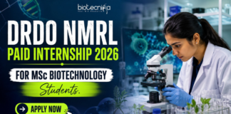 DRDO NMRL Paid Internship 2026 For MSc Biotechnology Students. Featured image showing a realistic biotechnology laboratory scene with a young female scientist using a microscope in a modern research lab. Bold text highlights “DRDO NMRL Paid Internship 2026 For MSc Biotechnology Students” with a bright neon-green and blue theme. The Biotecnika logo appears at the top center, while a large “Apply Now” button is placed prominently at the bottom. The design is vibrant, professional, and attention-grabbing, featuring biotech visuals such as DNA strands, lab equipment, and research elements to appeal to MSc Biotechnology students.