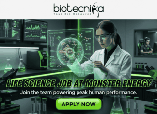 Exciting Life Science Job at Monster Energy | Don’t Miss This Opportunity Exciting Life Science Job at Monster Energy Don't Miss This. A job advertisement image with the header logo "biotecnika Your Bio Resource" and a stylized figure. The central scene is a detailed, futuristic laboratory with green lighting, where a female scientist in a lab coat interacts with a glowing hologram of an ATP molecule and "Human Performance Cell." Background monitors display biometric data and a separate room shows gamers and a person on a treadmill, symbolizing human performance research. Large bold text across the middle reads "LIFE SCIENCE JOB AT MONSTER ENERGY", followed by the subtext, "Join the team powering peak human performance." A prominent green "APPLY NOW" button is at the bottom center.