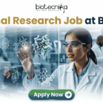 Latest Clinical Research Job at Baxter | Apply Now. A featured job advertisement banner for biotecnika, titled "Clinical Research Job at Baxter," set in a modern, futuristic laboratory. The visual focuses on a diverse female scientist, of South Asian or Indian descent, with safety glasses and a lab coat, who is interacting with and gesturing towards a floating, transparent holographic screen. The screen displays complex 3D molecular models of a protein and a drug, along with labels like 'Protein Drug Docking' and 'Data Docking'. In the blurred background, other researchers work with equipment and computer monitors in a well-equipped facility. At the top center is the "biotecnika Your Bio Resource" logo. At the bottom center, a prominent green button contains the text 'Apply Now' with a white arrow icon.