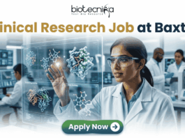 Latest Clinical Research Job for Life Science & Biomedical Graduates at Baxter | Apply Now Latest Clinical Research Job at Baxter | Apply Now. A featured job advertisement banner for biotecnika, titled "Clinical Research Job at Baxter," set in a modern, futuristic laboratory. The visual focuses on a diverse female scientist, of South Asian or Indian descent, with safety glasses and a lab coat, who is interacting with and gesturing towards a floating, transparent holographic screen. The screen displays complex 3D molecular models of a protein and a drug, along with labels like 'Protein Drug Docking' and 'Data Docking'. In the blurred background, other researchers work with equipment and computer monitors in a well-equipped facility. At the top center is the "biotecnika Your Bio Resource" logo. At the bottom center, a prominent green button contains the text 'Apply Now' with a white arrow icon.