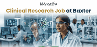 Latest Clinical Research Job at Baxter | Apply Now. A featured job advertisement banner for biotecnika, titled "Clinical Research Job at Baxter," set in a modern, futuristic laboratory. The visual focuses on a diverse female scientist, of South Asian or Indian descent, with safety glasses and a lab coat, who is interacting with and gesturing towards a floating, transparent holographic screen. The screen displays complex 3D molecular models of a protein and a drug, along with labels like 'Protein Drug Docking' and 'Data Docking'. In the blurred background, other researchers work with equipment and computer monitors in a well-equipped facility. At the top center is the "biotecnika Your Bio Resource" logo. At the bottom center, a prominent green button contains the text 'Apply Now' with a white arrow icon.