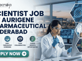 Scientist Job in Hyderabad for MSc Graduates | Aurigene Pharmaceutical Hiring Now Scientist Job for MSc Graduates at Aurigene Pharmaceutical. A professional corporate recruitment banner for a "SCIENTIST JOB AT AURIGENE PHARMACEUTICAL HYDERABAD" by Biotecnika. The image features a focused female scientist of Indian heritage in a lab coat and safety glasses, working with a multichannel pipette in a state-of-the-art pharmaceutical laboratory. The background shows a modern research facility with large windows overlooking a city skyline at dusk. Hexagonal frames to the right showcase a DNA helix, chemical glassware, and data analytics. Below the main headline, four icons highlight key aspects: Advanced Drug R&D, High-Throughput Screening, Team Collaboration, and Career Growth Opportunities. A prominent teal "APPLY NOW" button is positioned at the bottom left.