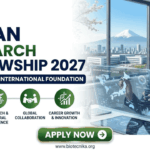 A professional promotional graphic from Biotecnika advertising the "Japan Research Fellowship 2027" at the "Matsumae International Foundation." The left side highlights four key benefits: full funding and allowance, research and cultural experience, global collaboration, and career growth and innovation. The right side shows a woman in a business suit interacting with a futuristic holographic display featuring a map of Japan and data charts. The background features office windows with a scenic view including a distant Mount Fuji and a cityscape with cherry blossom branches. At the bottom, a green "APPLY NOW" button and the website URL "www.biotecnika.org" are clearly visible.