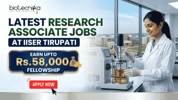 FI - 28052026 (1) Latest Research Associate Jobs at IISER Tirupati | Earn Upto Rs.58,000 Fellowship. A professional recruitment banner for "Latest Research Associate Jobs at IISER Tirupati," featuring the Biotecnika logo at the top left. On the right, a female scientist in a white lab coat and gloves is shown working with a laboratory bioreactor in a bright, modern lab setting. The background through a large window offers a realistic view of the IISER Tirupati campus. The left side of the image features the bold headline "LATEST RESEARCH ASSOCIATE JOBS AT IISER TIRUPATI." Below this, a prominent gold-framed blue box highlights the fellowship: "EARN UPTO Rs. 58,000 FELLOWSHIP" accompanied by an icon of a money bag. Three circular icons highlight key benefits: Conduct Advanced Bio-Research, Collaboration & Mentorship, and Career Growth Path. A large green "Apply Now" button with a white arrow and the website "biotecnika.org" are positioned at the bottom.