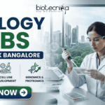 Biology Jobs at Merck in Bangalore | Apply Before It’s Gone Biology Jobs at Merck in Bangalore | Apply Before It's Gone. A Biotecnika recruitment banner advertising 'Biology Jobs' at 'Merck Bangalore.' On the right, a detailed photograph of a female scientist in a lab coat, safety glasses, and gloves meticulousy pipetting into a multi-well plate in a modern laboratory. The window behind her reveals a modern cityscape (Bangalore). The main text 'BIOLOGY JOBS' is stacked in large green and blue fonts, with 'AT MERCK BANGALORE' in a blue bar below it. Below the text, three circular icons with descriptive text list focus areas: 'ADVANCED DRUG DISCOVERY,' 'CELL LINE DEVELOPMENT,' and 'GENOMICS & PROTEOMICS.' The Biotecnika logo is in the top corner, and a prominent green 'APPLY NOW' button with a right arrow is at the bottom-left.