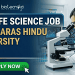BSc Life Science Job at Banaras Hindu University | Apply Now. A professional featured image for a "BSc LIFE SCIENCE JOB at BANARAS HINDU UNIVERSITY (BHU)." The image depicts a female scientist in a white lab coat and safety goggles using a microscope and pipette in a modern laboratory. The Biotecnika logo is at the top center, and a bright green "APPLY NOW" button with a cursor icon is at the bottom left. The background features scientific data on monitors, laboratory glassware with colorful liquids, and a DNA helix graphic.
