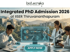 Integrated PhD Admission 2026 at IISER Thiruvananthapuram. An inspiring featured image for Integrated PhD admission, featuring three students in lab coats collaborating in a modern IISER Thiruvananthapuram laboratory during golden hour. Large text at the top reads: "Integrated PhD Admission 2026 at IISER Thiruvananthapuram", with the Biotecnika logo. Below, students are pointing at a transparent screen with DNA structures and using a microscope, with a witty "Caffeine & CRISPR" mug. A large teal "APPLY NOW" button is at the bottom center.