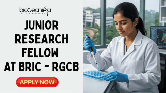 Junior Research Fellow Vacancy 2026 at BRIC – RGCB Earn ₹37,000 Salary Junior Research Fellow Vacancy 2026 at BRIC – RGCB Earn ₹37,000 Salary. A featured job advertisement image for a Junior Research Fellow position at BRIC-RGCB. At the top center is the biotecnika Your Bio Resource logo. The image features a young woman researcher in a lab coat and gloves, seated at a modern lab bench and carefully pipetting into a microplate. Surrounding her are lab equipment and a monitor showing scientific data. Large glass windows in the background look out onto a modern research campus with greenery. A prominent central text overlay reads, "JUNIOR RESEARCH FELLOW VACANCY at BRIC – RGCB". At the bottom center is a green button that says "APPLY NOW".