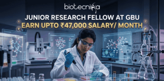 Junior Research Fellow at GBU Earn Upto ₹47,000 Salary Month. A job advertisement featuring a female researcher in a modern drug research lab, using a multi-channel pipette, surrounded by transparent screens displaying 3D molecular structures. Prominent text at the top reads: "JUNIOR RESEARCH FELLOW AT GBU", followed by a central banner stating: "EARN UPTO ₹47,000 SALARY/ MONTH". The biotecnika logo is at the very top, and a blue button at the bottom says: "APPLY NOW".