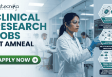 Latest Clinical Research Jobs at Amneal | Apply Before It Closes! Latest Clinical Research Jobs at Amneal Apply Before It Closes! A professional corporate recruitment banner for "CLINICAL RESEARCH JOBS AT AMNEAL" featuring the Biotecnika logo. The image showcases a focused female scientist of Indian heritage in a white lab coat and safety goggles, interacting with a high-tech digital monitor displaying clinical trial data and ECG waveforms. To the right, hexagonal icons highlight key clinical research themes: "Continuous Patient Monitoring," "Multi-modal Data Integration," and "Accelerated Study Timelines." The background depicts a modern, brightly lit clinical facility with other researchers at work. A prominent green "APPLY NOW" button with a white arrow is positioned at the bottom left.