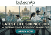 Latest Life Science Job at Thermo Fisher Scientific Bangalore | Apply Online Here Latest Life Science Job at Thermo Fisher Scientific Bangalore Apply Online Here. An attractive job advertisement banner from Biotecnika, featuring three scientists in white lab coats actively working in a modern laboratory. In the background, visible through a large window, is the recognizable Vidhana Soudha building in Bengaluru. Prominent text overlay reads: "LATEST LIFE SCIENCE JOB at THERMO FISHER SCIENTIFIC BANGALORE". At the top is the Biotecnika logo, and at the bottom center is a "APPLY NOW" button. A "NEW OPENING" handshake badge is in the top right.