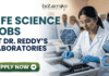 Life Science Jobs at Dr. Reddy’s Laboratories | BSc & MSc Candidates Apply Now! Life Science Jobs at Dr. Reddy's Laboratories BSc & MSc Candidates Apply Now! A professional corporate recruitment banner for "LIFE SCIENCE JOBS AT DR. REDDY'S LABORATORIES" featuring the Biotecnika logo at the top. The image depicts a focused female scientist of Indian heritage wearing a white lab coat, safety goggles, and blue gloves, working with a modern automated liquid handling system and microplates. Hexagonal graphics to the right showcase scientific concepts like a DNA helix labeled 'CRISPR', a microfluidic chip, and a biological cell. In the background, a team of researchers is visible in a clean, state-of-the-art laboratory environment. A prominent green "APPLY NOW" button with a white arrow is located at the bottom left.