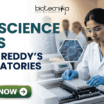 Life Science Jobs at Dr. Reddy’s Laboratories | BSc & MSc Candidates Apply Now! Life Science Jobs at Dr. Reddy's Laboratories BSc & MSc Candidates Apply Now! A professional corporate recruitment banner for "LIFE SCIENCE JOBS AT DR. REDDY'S LABORATORIES" featuring the Biotecnika logo at the top. The image depicts a focused female scientist of Indian heritage wearing a white lab coat, safety goggles, and blue gloves, working with a modern automated liquid handling system and microplates. Hexagonal graphics to the right showcase scientific concepts like a DNA helix labeled 'CRISPR', a microfluidic chip, and a biological cell. In the background, a team of researchers is visible in a clean, state-of-the-art laboratory environment. A prominent green "APPLY NOW" button with a white arrow is located at the bottom left.