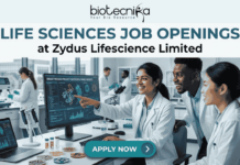 Life Sciences Job Openings at Zydus Lifescience Limited | Walk-In Interview 2026 Life Sciences Job Openings at Zydus Lifescience Limited Walk-In Interview 2026. A promotional banner from Biotecnika, titled 'LIFE SCIENCES JOB OPENINGS at Zydus Lifescience Limited'. The image features a photo of three diverse and collaborative researchers in a modern laboratory. One woman in a lab coat is smiling and pointing to a computer monitor displaying 'SUCCESSFUL PHASE III RESULTS' and scientific data visualizations. Her colleagues look on with interest. Laboratory tools like pipettes, petri dishes with samples, vials, and a laptop are visible on the desk. At the bottom center, a prominent blue button reads 'APPLY NOW' with an arrow icon. The overall theme is successful, modern scientific collaboration.