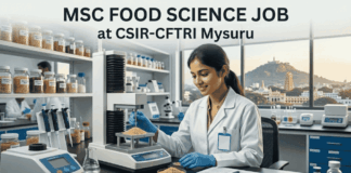 MSc Food Science Job at CSIR-CFTRI Mysuru | Apply Before Deadline! MSc Food Science Job at CSIR-CFTRI Apply Online. A realistic photograph with text overlay at the top: 'MSC FOOD SCIENCE JOB at CSIR-CFTRI Mysuru.' A smiling female food scientist in a white lab coat and gloves is depicted operating a grain analysis machine in a laboratory. The well-stocked shelves behind her hold numerous jars of cereal samples and lab equipment. In the background, a large window frames the view of the city of Mysuru, including a distinctive temple gopuram on Chamundi Hill under a warm sky. At the bottom, a prominent blue button states 'APPLY NOW'."
