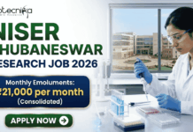 NISER Bhubaneswar Research Job 2026 – Life Sciences Graduates Can Apply NISER Bhubaneswar Research Job 2026 – Life Sciences Graduates Can Apply. A professional recruitment banner for "NISER Bhubaneswar Research Job 2026," featuring the Biotecnika logo at the top left. On the right, a female scientist in a white lab coat and blue gloves is precisely using a pipette on a multi-well plate in a bright, modern laboratory. The left side displays the bold headline "NISER BHUBANESWAR RESEARCH JOB 2026." Below the title, a prominent gold-framed blue box highlights the salary: "Monthly Emoluments: ₹21,000 per month (Consolidated)." The background through the lab window shows a realistic view of the NISER Bhubaneswar campus. A large green "Apply Now" button with a white arrow is positioned at the bottom left.