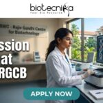 PhD Admission 2026 at BRIC-RGCB | Unlock Your Life Science Career Dream! PhD Admission 2026 at BRIC-RGCB Unlock Your Life Science Career Dream! Promotional banner for Biotecnika, "Your Bio Resource," advertising PhD Admission 2026 at BRIC-RGCB (Rajiv Gandhi Centre for Biotechnology). The central image is of a female scientist in safety glasses and a lab coat working with advanced lab equipment and a large computer monitor displaying DNA and protein visualizations. In the background, a sign on a glass partition reads "BRIC - Rajiv Gandhi Centre for Biotechnology," and a modern research campus is visible through windows. At the bottom, a prominent green button with white text says "APPLY NOW."