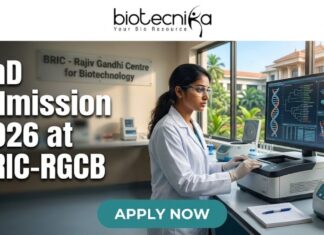 PhD Admission 2026 at BRIC-RGCB Unlock Your Life Science Career Dream! Promotional banner for Biotecnika, "Your Bio Resource," advertising PhD Admission 2026 at BRIC-RGCB (Rajiv Gandhi Centre for Biotechnology). The central image is of a female scientist in safety glasses and a lab coat working with advanced lab equipment and a large computer monitor displaying DNA and protein visualizations. In the background, a sign on a glass partition reads "BRIC - Rajiv Gandhi Centre for Biotechnology," and a modern research campus is visible through windows. At the bottom, a prominent green button with white text says "APPLY NOW."