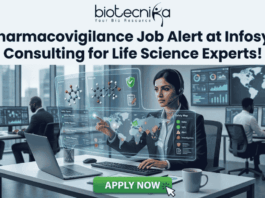 Pharmacovigilance Job Alert at Infosys Consulting for Life Science Experts! A job advertisement graphic with text at the top that reads: "biotecnika" and "Your Bio Resource" with a stylized icon, followed by the headline, "Pharmacovigilance Job Alert at Infosys Consulting for Life Science Experts!". The central image shows a woman of South Asian descent wearing a headset, seated at a desk with a laptop in a modern office setting. She is looking at and reaching toward a futuristic, transparent data display interface with molecular structures, a world map, data charts, and labels like "Safety Reports," "Product Reports," and a "Safety Map" legend indicating colored zones for alert, warning, and safety. Other employees are working at desks in the background of a glass-walled high-rise office. At the bottom center, there is a large green button with white text that reads "APPLY NOW", and a hand cursor is clicking it.