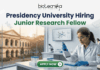 Presidency University Hiring Junior Research Fellow | Earn Upto ₹25,000 Salary! Presidency University Hiring Junior Research Fellow Earn Upto ₹25,000 Salary! A recruitment banner for Presidency University featuring the text 'Presidency University Hiring Junior Research Fellow' at the top, along with the 'biotecnika' logo. On the left side, the iconic colonial architecture of Presidency University's building is visible through a window, with a view of the sun setting. The right side features a female Indian scientist of a professional and focused appearance, wearing a lab coat, safety glasses, and blue gloves, meticulously using a pipette to fill a well-plate. She is surrounded by modern laboratory equipment, including a microscope and a monitor displaying molecular structures. Floating icons of DNA double helices are subtly placed around the text area. An 'APPLY NOW' button is prominent at the bottom center.