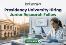 Presidency University Hiring Junior Research Fellow | Earn Upto ₹25,000 Salary! Presidency University Hiring Junior Research Fellow Earn Upto ₹25,000 Salary! A recruitment banner for Presidency University featuring the text 'Presidency University Hiring Junior Research Fellow' at the top, along with the 'biotecnika' logo. On the left side, the iconic colonial architecture of Presidency University's building is visible through a window, with a view of the sun setting. The right side features a female Indian scientist of a professional and focused appearance, wearing a lab coat, safety glasses, and blue gloves, meticulously using a pipette to fill a well-plate. She is surrounded by modern laboratory equipment, including a microscope and a monitor displaying molecular structures. Floating icons of DNA double helices are subtly placed around the text area. An 'APPLY NOW' button is prominent at the bottom center.