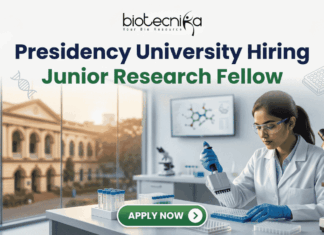 Presidency University Hiring Junior Research Fellow | Earn Upto ₹25,000 Salary! Presidency University Hiring Junior Research Fellow Earn Upto ₹25,000 Salary! A recruitment banner for Presidency University featuring the text 'Presidency University Hiring Junior Research Fellow' at the top, along with the 'biotecnika' logo. On the left side, the iconic colonial architecture of Presidency University's building is visible through a window, with a view of the sun setting. The right side features a female Indian scientist of a professional and focused appearance, wearing a lab coat, safety glasses, and blue gloves, meticulously using a pipette to fill a well-plate. She is surrounded by modern laboratory equipment, including a microscope and a monitor displaying molecular structures. Floating icons of DNA double helices are subtly placed around the text area. An 'APPLY NOW' button is prominent at the bottom center.