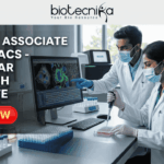 Project Associate Job at MACS - Agharkar Research Institute. A detailed job advertisement graphic for a Project Associate position at MACS - Agharkar Research Institute in Pune, India, from Biotecnika, 'Your Bio Resource'. The left side displays bold text. On the right, a photograph shows two masked scientists in a modern laboratory, one pointing to a screen with colorful cellular images and the other using a pipette. A teal button at the bottom reads 'Apply Now'.