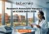 Research Associate Vacancy at ICGEB Delhi 2026 | PhD Candidates Apply Now Research Associate Vacancy at ICGEB Delhi 2026 PhD Candidates Apply Now. A promotional banner image for a job opening. The top center features the text logo "biotecnika - Your Bio Resource." Below it, a large headline reads "Research Associate Vacancy at ICGEB Delhi 2026." On the right, a female scientist in a white lab coat and glasses holds a well plate with colored samples, looking up at it. The setting is a modern biotechnology lab. On the counter on the left, there is lab equipment, including a piece labeled "ICGEB DELHI." Through a large window in the background, a red-brick university campus is visible, with a sign reading "ICGEB Delhi." An orange-red call-to-action button at the bottom center says "APPLY NOW" with a right arrow icon.