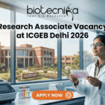 Research Associate Vacancy at ICGEB Delhi 2026 | PhD Candidates Apply Now Research Associate Vacancy at ICGEB Delhi 2026 PhD Candidates Apply Now. A promotional banner image for a job opening. The top center features the text logo "biotecnika - Your Bio Resource." Below it, a large headline reads "Research Associate Vacancy at ICGEB Delhi 2026." On the right, a female scientist in a white lab coat and glasses holds a well plate with colored samples, looking up at it. The setting is a modern biotechnology lab. On the counter on the left, there is lab equipment, including a piece labeled "ICGEB DELHI." Through a large window in the background, a red-brick university campus is visible, with a sign reading "ICGEB Delhi." An orange-red call-to-action button at the bottom center says "APPLY NOW" with a right arrow icon.