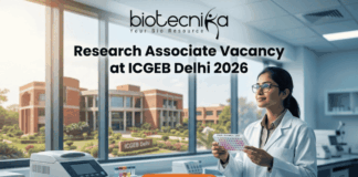 Research Associate Vacancy at ICGEB Delhi 2026 | PhD Candidates Apply Now Research Associate Vacancy at ICGEB Delhi 2026 PhD Candidates Apply Now. A promotional banner image for a job opening. The top center features the text logo "biotecnika - Your Bio Resource." Below it, a large headline reads "Research Associate Vacancy at ICGEB Delhi 2026." On the right, a female scientist in a white lab coat and glasses holds a well plate with colored samples, looking up at it. The setting is a modern biotechnology lab. On the counter on the left, there is lab equipment, including a piece labeled "ICGEB DELHI." Through a large window in the background, a red-brick university campus is visible, with a sign reading "ICGEB Delhi." An orange-red call-to-action button at the bottom center says "APPLY NOW" with a right arrow icon.