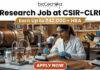 Research Job at CSIR-CLRI | Earn Up to ₹42,000 + HRA | Apply Before Deadline Research Job at CSIR-CLRI Earn Up to ₹42,000 + HRA. A promotional banner advertisement from Biotecnika, titled "Research Job at CSIR-CLRI", featuring a prominent gold banner with text that reads: "Earn Up to ₹42,000 + HRA". The main image shows a female scientist in a lab coat, safety glasses, and blue gloves, using a stereo microscope to analyze a textured material sample (likely a leather sample, given CLRI's focus). She is at a laboratory bench equipped with other microscopes, glass apparatus with samples, chemical bottles, and a computer monitor showing data. In the background are larger industrial lab machines. The Biotecnika "Your Bio Resource" logo is at the top center. At the bottom, a red button with white text reads: "APPLY NOW".