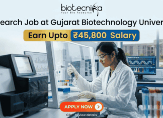 Research Job at Gujarat Biotechnology University ₹45,800 Salary. A promotional graphic for a Research Job at Gujarat Biotechnology University, featuring the 'biotecnika - Your Bio Resource' logo at the top. The main headline reads 'Research Job at Gujarat Biotechnology University' with prominent boxes below highlighting 'Earn Upto ₹45,800 Salary'. The background is a photograph of a female researcher in a white lab coat, gloves, and safety glasses, actively pipetting a multi-well plate within a modern, well-equipped genetics laboratory. Sophisticated sequencing equipment and monitors displaying DNA chromatograms and data are visible, along with a view of a university building through a window. A large, red 'APPLY NOW' button is at the bottom center with the text 'Click to view details'.