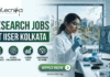Top Research Jobs for MSc Life Science Candidates in India at IISER Kolkata Research Jobs at IISER Kolkata. A professional recruitment banner for "Research Jobs at IISER Kolkata," featuring the Biotecnika logo at the top left. On the right, a female scientist wearing safety glasses and blue gloves is using a multichannel pipette at a lab bench. Next to her is a curved monitor displaying advanced data and molecular visualizations, with a 3D DNA helix floating in the foreground. The left side features the bold headline "RESEARCH JOBS AT IISER KOLKATA" and four circular icons highlighting: Innovative Bio-sciences, Global Collaboration, Career Path, and Mentorship Network. The background through a large window provides a realistic view of the IISER Kolkata campus buildings. A prominent green "Apply Now" button and the website "biotecnika.org" are located at the bottom.