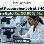 Latest Researcher Job at JNCASR | Earn Upto Rs. 56,000/ Month Researcher Job at JNCASR 2026 Life Science Career. An advertisement banner for a Researcher Job at JNCASR, featuring a female scientist in a lab coat using a microscope in a laboratory. Key text states: "Latest Researcher Job at JNCASR", "Earn Upto Rs. 56,000/ Month", with a prominent "APPLY NOW" button at the bottom and a "biotecnika" logo at the top.