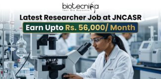 Latest Researcher Job at JNCASR | Earn Upto Rs. 56,000/ Month Researcher Job at JNCASR 2026 Life Science Career. An advertisement banner for a Researcher Job at JNCASR, featuring a female scientist in a lab coat using a microscope in a laboratory. Key text states: "Latest Researcher Job at JNCASR", "Earn Upto Rs. 56,000/ Month", with a prominent "APPLY NOW" button at the bottom and a "biotecnika" logo at the top.