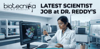 Latest Scientist Job at Dr. Reddy’s | MSc Food Science Job Opportunity Scientist Job at Dr. Reddy’s MSc Food Science Job. A detailed job advertisement image for a scientist position. At the top-left is the biotecnika logo 'biotecnika Your Bio Resource'. Large headline text to the top-right reads: 'LATEST SCIENTIST JOB at DR. REDDY'S'. The central scene features a focused female scientist, 'Dr. A. Rao, R&D Lead', in a modern, high-tech pharmaceutical research laboratory. She is working at a computer station, using a multi-channel pipette on a multi-well plate. Her monitor displays complex 3D molecular visualizations of protein structures, with text labels like 'KINASE TARGET LEAD OPTIMIZATION' and 'CONFIRMATION OF BINDING SUCCESSFUL'. The extensive lab background shows automated equipment, analytical tools, and a view of a modern city from a window. A coffee mug and a sticky note reading 'Potential breakthrough kinase data' are on the desk. A prominent blue 'APPLY NOW' button is at the bottom center.