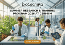 Summer Research & Training Program 2026 At CSIR-IIIM | Limited Seats for Life Science Students Summer Research & Training Program 2026 at CSIR-IIIM. A featured image for a job page set in a sunlit, modern research greenhouse. The interior is filled with flourishing green plants in raised beds. Four scientists in white lab coats are working among the flora. In the foreground, a South Asian man uses a pipette with a microplate on an illuminated screen-table. Beside him, another man holds a tablet displaying a linked molecular model near a microscope. In the background, a Black woman and another scientist work further back among lab equipment and plants. Light streams in through the glass walls and roof. The 'biotecnika Your Bio Resource' logo is at the top center. Large text on a central dark band reads: 'SUMMER RESEARCH & TRAINING PROGRAM 2026 AT CSIR-IIIM'. An orange button at the bottom center reads: 'APPLY NOW'. The overall scene is bright, collaborative, and scientifically focused.