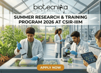 Summer Research & Training Program 2026 At CSIR-IIIM | Limited Seats for Life Science Students Summer Research & Training Program 2026 at CSIR-IIIM. A featured image for a job page set in a sunlit, modern research greenhouse. The interior is filled with flourishing green plants in raised beds. Four scientists in white lab coats are working among the flora. In the foreground, a South Asian man uses a pipette with a microplate on an illuminated screen-table. Beside him, another man holds a tablet displaying a linked molecular model near a microscope. In the background, a Black woman and another scientist work further back among lab equipment and plants. Light streams in through the glass walls and roof. The 'biotecnika Your Bio Resource' logo is at the top center. Large text on a central dark band reads: 'SUMMER RESEARCH & TRAINING PROGRAM 2026 AT CSIR-IIIM'. An orange button at the bottom center reads: 'APPLY NOW'. The overall scene is bright, collaborative, and scientifically focused.