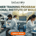 Summer Training Program 2026 at National Institute of Biologicals | Biotechnology Students Can Apply Now! Summer Training Program 2026 at National Institute of Biologicals. A promotional graphic for the "SUMMER TRAINING PROGRAM 2026 AT NATIONAL INSTITUTE OF BIOLOGICALS", presented by biotecnika. Text at the top is green. The main image shows a diverse group of scientists and trainees working in a well-equipped laboratory. A central woman scientist is focused on a microscope, a male scientist works with liquid samples, and other figures are in the background. Equipment includes computer monitors with DNA graphics, test tubes, and a centrifuge labeled "National Institute of Biologicals (NIB), Noida". A large orange "APPLY NOW" button is at the bottom.