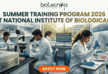 Summer Training Program 2026 at National Institute of Biologicals | Biotechnology Students Can Apply Now! Summer Training Program 2026 at National Institute of Biologicals. A promotional graphic for the "SUMMER TRAINING PROGRAM 2026 AT NATIONAL INSTITUTE OF BIOLOGICALS", presented by biotecnika. Text at the top is green. The main image shows a diverse group of scientists and trainees working in a well-equipped laboratory. A central woman scientist is focused on a microscope, a male scientist works with liquid samples, and other figures are in the background. Equipment includes computer monitors with DNA graphics, test tubes, and a centrifuge labeled "National Institute of Biologicals (NIB), Noida". A large orange "APPLY NOW" button is at the bottom.