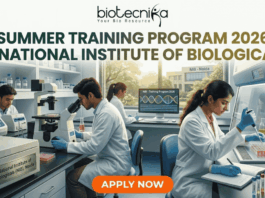 Summer Training Program 2026 at National Institute of Biologicals. A promotional graphic for the "SUMMER TRAINING PROGRAM 2026 AT NATIONAL INSTITUTE OF BIOLOGICALS", presented by biotecnika. Text at the top is green. The main image shows a diverse group of scientists and trainees working in a well-equipped laboratory. A central woman scientist is focused on a microscope, a male scientist works with liquid samples, and other figures are in the background. Equipment includes computer monitors with DNA graphics, test tubes, and a centrifuge labeled "National Institute of Biologicals (NIB), Noida". A large orange "APPLY NOW" button is at the bottom.