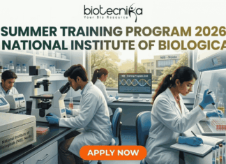 Summer Training Program 2026 at National Institute of Biologicals | Biotechnology Students Can Apply Now! Summer Training Program 2026 at National Institute of Biologicals. A promotional graphic for the "SUMMER TRAINING PROGRAM 2026 AT NATIONAL INSTITUTE OF BIOLOGICALS", presented by biotecnika. Text at the top is green. The main image shows a diverse group of scientists and trainees working in a well-equipped laboratory. A central woman scientist is focused on a microscope, a male scientist works with liquid samples, and other figures are in the background. Equipment includes computer monitors with DNA graphics, test tubes, and a centrifuge labeled "National Institute of Biologicals (NIB), Noida". A large orange "APPLY NOW" button is at the bottom.