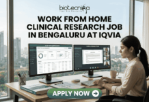 Work From Home Clinical Research Job in Bengaluru at IQVIA | Apply Now Work From Home Clinical Research Job in Bengaluru at IQVIA. A professional job advertisement banner for a "Work From Home Clinical Research Job in Bengaluru at IQVIA." The image features the Biotecnika logo at the top and a central headline in bold text. Below the text, a woman is shown working at a modern desk with a scenic city skyline view in the background. She is using a dual-monitor setup displaying clinical trial data management software and a video conference with a research team. A prominent green "Apply Now" button with a white arrow is located at the bottom center.