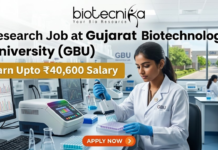 ₹40,600 Salary Research Job at Gujarat Biotechnology University (GBU) | JRF & SRF Openings ₹40,600 Salary Research Job at Gujarat Biotechnology University (GBU) JRF & SRF Openings. A focused female researcher in a white lab coat uses a multi-channel pipette on a microplate within a modern GBU laboratory. Large bold text reads: 'Research Job at Gujarat Biotechnology University (GBU)'. A yellow banner highlights 'Earn Upto ₹40,600 Salary'. The Biotecnika logo is at the top. The background features GBU lab equipment, a monitor with DNA graphs, another researcher, and GBU campus views. At the bottom center is an orange 'APPLY NOW' button with a right arrow.