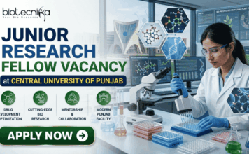 ₹42,000 Salary Junior Research Fellow Vacancy at Central University of Punjab ₹42,000 Salary Junior Research Fellow Vacancy at Central University of Punjab. A corporate recruitment banner for a "JUNIOR RESEARCH FELLOW VACANCY at CENTRAL UNIVERSITY OF PUNJAB" featuring the Biotecnika logo. The image showcases a focused female scientist of Indian heritage wearing a lab coat and safety glasses, using a multichannel pipette on a well-plate. The background features the modern architecture of the university and laboratory monitors displaying genetic and bio-prospecting data. Four circular green icons highlight key job features: Drug Development & Optimization, Cutting-Edge Bio Research, Mentorship & Collaboration, and Modern Punjab Facility. A prominent green "APPLY NOW" button is located at the bottom left.