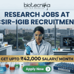 ₹42,000 Salary Research Jobs at Institute of Life Sciences | Apply Now ₹42,000 Salary Research Jobs at Institute of Life Sciences Apply Now. A job recruitment banner from Biotecnika for CSIR-IGIB. The headline reads 'RESEARCH JOBS AT CSIR-IGIB RECRUITMENT'. A female scientist in a lab coat uses a multi-channel pipette. The desk features beakers, a box of 'DRUG CANDIDATE' vials, and a monitor with a 3D molecular structure. A campus of buildings is visible through a large window. A gold banner highlights 'GET UPTO ₹42,000 SALARY/ MONTH'. An 'Apply Now' button is at the bottom.
