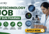 Biotechnology Job at Sun Pharma | Opportunity for MSc & MTech Candidates Biotechnology Job at Sun Pharma Opportunity for MSc & MTech Candidates. A professional promotional banner for a "Biotechnology Job at Sun Pharma." The top left displays the Biotecnika logo. The main header text boldly reads "BIOTECHNOLOGY JOB AT SUN PHARMA" in a green and dark color scheme. Below the title, four circular green icons are labeled: "ADVANCED R&D", "DRUG DISCOVERY", "GENETIC INNOVATION", and "CAREER PATHS". In the center, three floating circular graphics illustrate a DNA double helix, a colorful protein model, and a biochip. On the right side, a female researcher wearing a white lab coat and safety glasses works attentively with a laboratory bioreactor containing a golden liquid, set against a bright, modern pharmaceutical lab background. A prominent gold "APPLY NOW" button with an arrow sits at the bottom center-right.