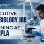 Executive Microbiology Job Opening at Cipla – MSc Candidates Apply Now. A professional corporate recruitment banner for Cipla, sized 1920x1080 pixels with a blue gradient color scheme. On the left, bold text reads "EXECUTIVE MICROBIOLOGY JOB OPENING at Cipla," with "MICROBIOLOGY JOB" and "Cipla" prominently highlighted. On the right, a male microbiologist wearing a white lab coat, safety glasses, and blue gloves is focused on using a microscope in a clean, modern laboratory setting. The Cipla logo is positioned in the top right corner, and a distinct blue "Apply Now" button sits in the bottom right corner.
